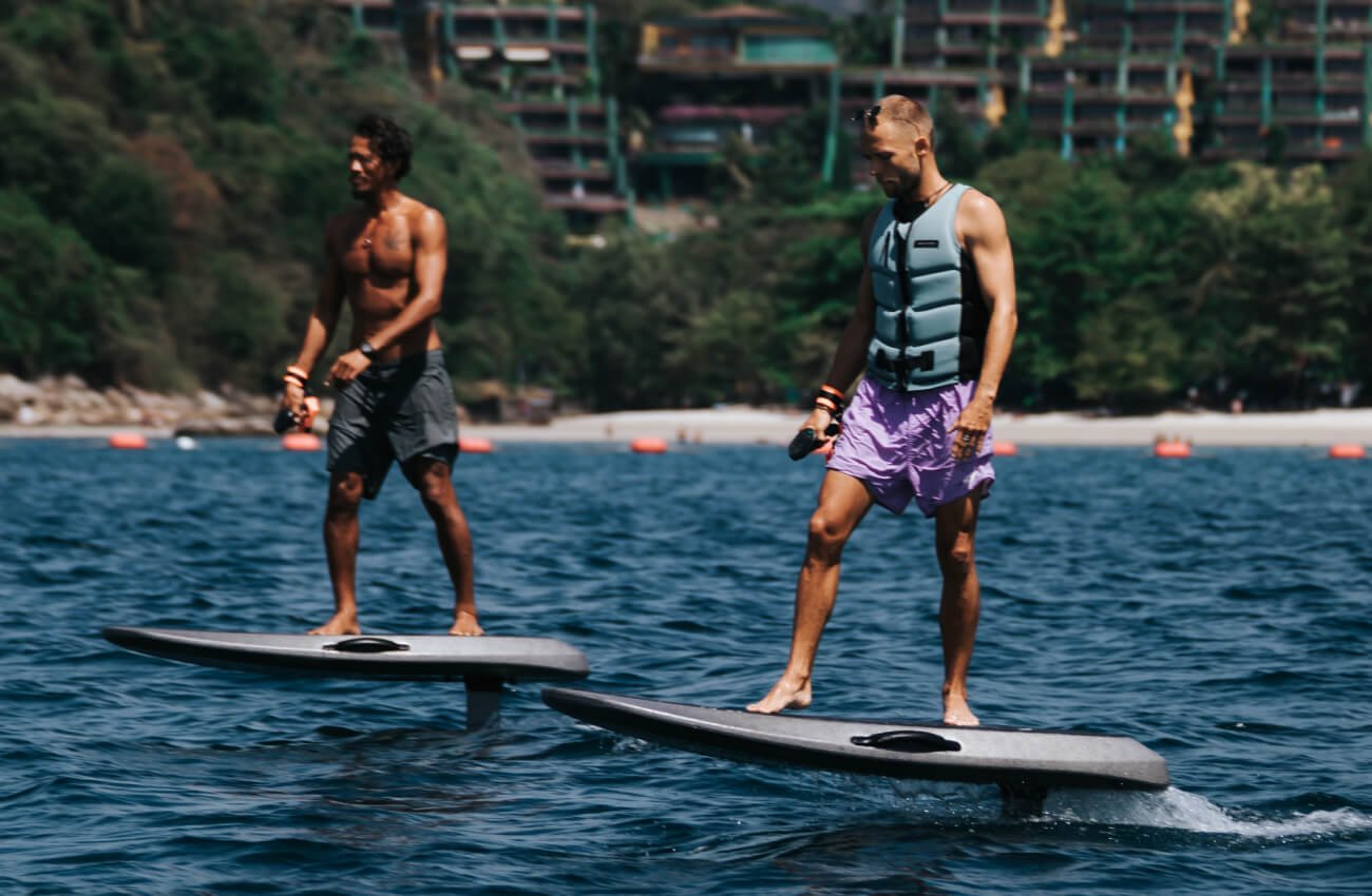 Two guys cruising near the shore on flying surfboards